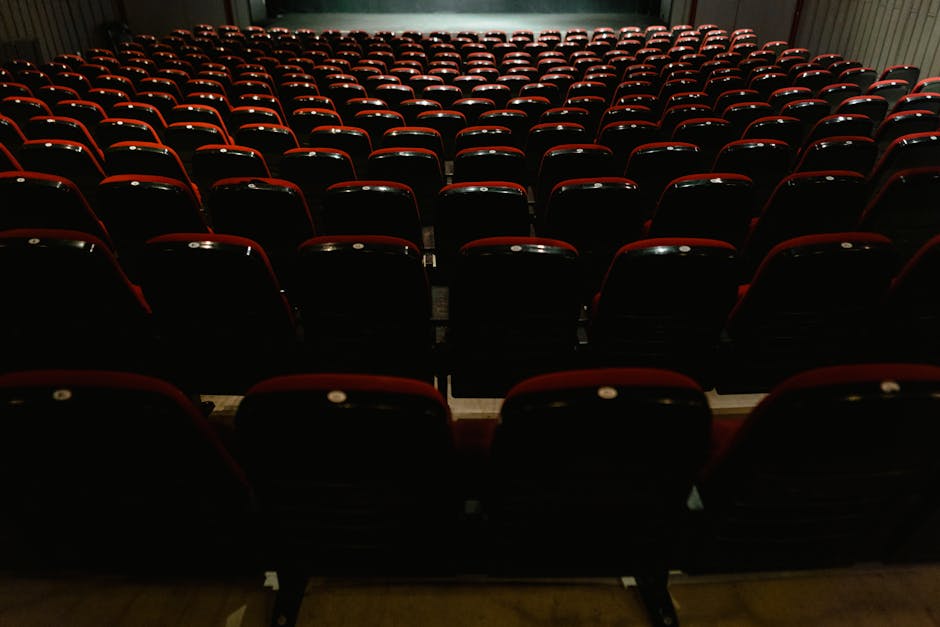 An empty movie theater interior with rows of red and black seats, awaiting audience.
